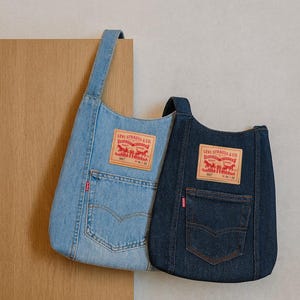 May include: Two denim tote bags, one light blue and one dark blue, with the Levi Strauss & Co. logo patch. Each bag has a pocket and a handle. The bags are made from recycled denim.