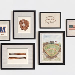 May include: A gallery wall set of six black-framed prints featuring baseball-themed illustrations. The artwork includes a letter M, a baseball glove with a ball, two wooden bats, a stadium view, an American flag, and the text Long Live Boyhood.