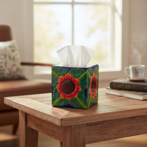 May include: A square ceramic tissue box cover featuring a hand-painted sunflower motif with vibrant orange and red petals, a dark brown center, and green leaves against a deep blue background, with white tissues extending from the top opening.