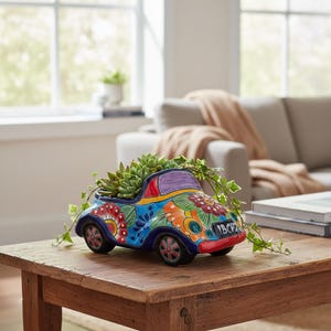 May include: A ceramic car-shaped planter painted in vibrant blue, red, orange, and green with intricate floral patterns. The vehicle features a purple windshield, black wheels with red accents, and a license plate reading 1BCH2, holding a green succulent.