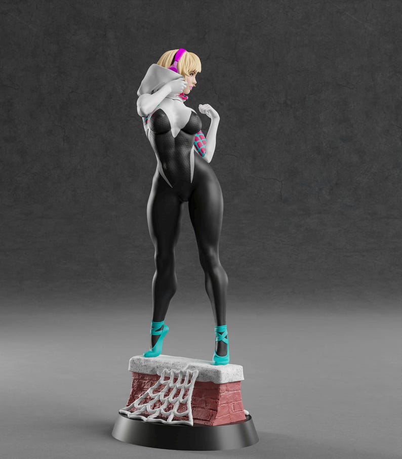 K&ouml;nnte beinhalten: Figur einer Superheldin in einem schwarz-wei&szlig;en Anzug, die auf einer Ziegelstruktur steht. Die Figur hat blondes Haar, ein rosa Stirnband und t&uuml;rkisfarbene High Heels. Der Sockel hat ein Spinnennetz-Design.