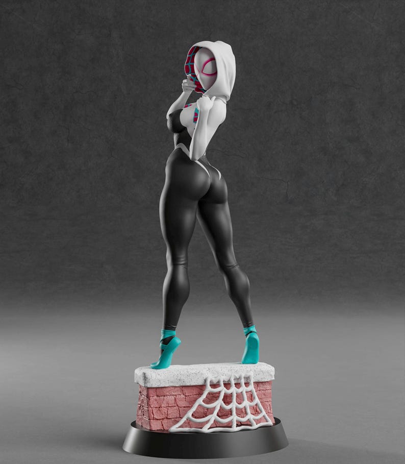 K&ouml;nnte beinhalten: Figur einer Superheldin in einem schwarz-wei&szlig;en Body, t&uuml;rkisfarbenen Abs&auml;tzen und einer wei&szlig;en Kapuzenmaske. Die Figur steht auf einem ziegelartigen Sockel mit einem wei&szlig;en Spinnennetz-Design. Der Hintergrund ist einfarbig grau.