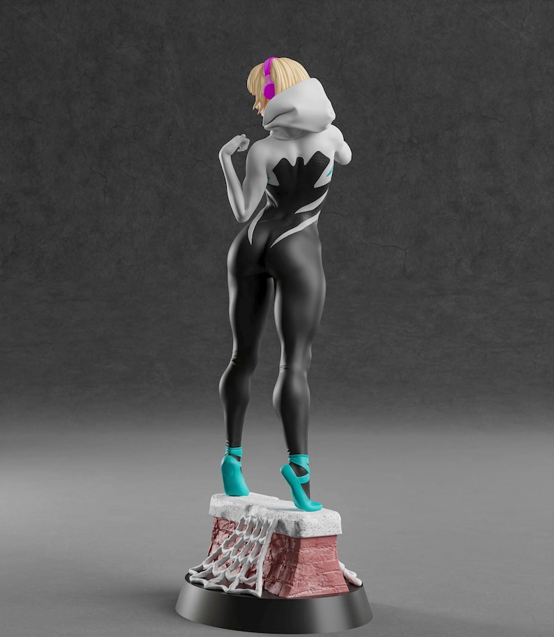 K&ouml;nnte beinhalten: Figur einer Superheldin in einem schwarz-wei&szlig;en Body mit Kapuze. Die Figur steht auf einem rot-wei&szlig;en Sockel mit Spinnennetz-Design. Sie tr&auml;gt t&uuml;rkisfarbene Ballettschuhe und hat blondes Haar.