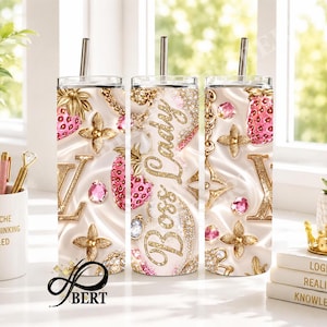 May include: Three stainless steel tumblers with straws, featuring a white background with gold accents, pink strawberries, and the words "Boss Lady". The tumblers are decorated with gold chains, floral designs, and the letter "V".