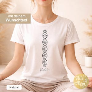 Könnte beinhalten: Weißes T-Shirt mit einem vertikalen Chakra-Design in Grau und dem Wort "Kundalini" in Schreibschrift. Das Shirt hat auch den Text "mit deinem Wunschtext" in einer beigen Box. Teil der "Natural"-Kollektion.