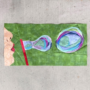 Op de afbeelding: Een gequilt textielkunstwerk met een persoon die bellen blaast. De bellen zijn gemaakt van blauwe, paarse en groene stoffen. De achtergrond is een groen textiel met textuur, en een rood rietje is zichtbaar.