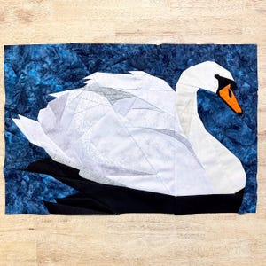 May include: A white swan with a black beak and orange accents is made from fabric pieces and sewn together. The swan is on a blue background.