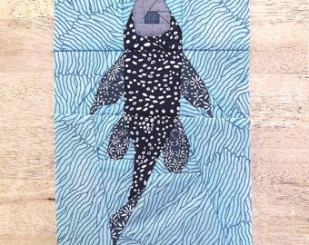 May include: A fabric art piece featuring a stylized black and white spotted creature with floral accents, set against a light blue wavy background. The artwork is rectangular and appears to be a quilt block.