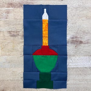 Puede incluir: Un bloque de tela azul con una aplicación verde, roja y blanca de una bombilla de Navidad.