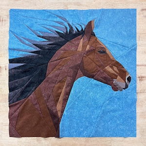 May include: A fabric art piece featuring a horse's head in profile. The horse is rendered in shades of brown, with a black mane and a blue background. The design is geometric, with the horse's form created from various fabric shapes.