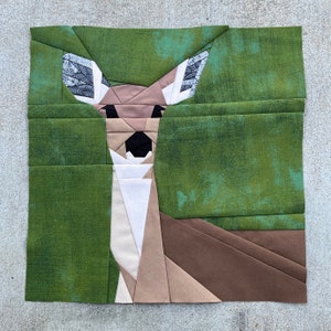 Könnte beinhalten: Eine grüne Patchwork-Decke aus Stoff mit einem Hirsch-Motiv. Der Hirsch besteht aus braunen, weißen und grauen Stoffstücken.