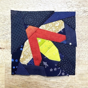 May include: A square patchwork design made from fabric pieces in a variety of colours and patterns. The design incorporates red, yellow, blue, and gold fabrics. The patchwork is constructed from small fabric pieces sewn together to create a unique design.