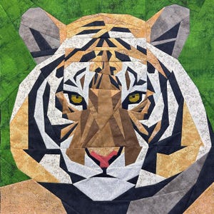 May include: A close-up of a tiger's face, created with a patchwork of fabric in various shades of brown, black, white, and beige. The tiger's face is symmetrical and features a large, black nose, a pink mouth, and two large, yellow eyes.