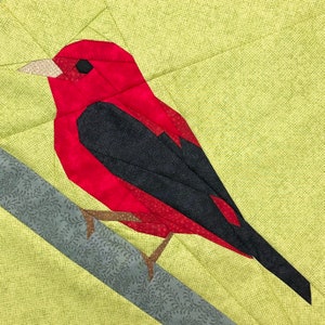 Könnte beinhalten: Ein roter und schwarzer Vogel mit langem Schnabel, der auf einem Ast sitzt. Der Vogel ist aus Stoff und Teil eines Quiltblocks.