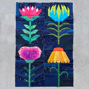 May include: A patchwork fabric panel with four stylised flowers in pink, blue, yellow, and orange. The flowers have green stems and leaves, set against a dark blue patchwork background. A handmade textile art piece.