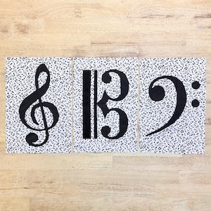 May include: Three black and white musical note symbols on a white background with a black musical note pattern. The symbols are a treble clef, a bass clef, and a bass clef.