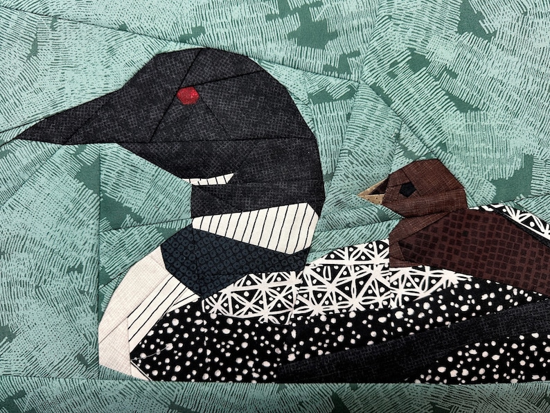 Peut inclure: Une &oelig;uvre d'art textile repr&eacute;sentant un huard et son petit. Le huard adulte a une t&ecirc;te et un cou noirs avec un &oelig;il rouge, et une poitrine &agrave; motifs blancs et noirs. Le petit est brun. Le fond est de couleur vert d'eau.