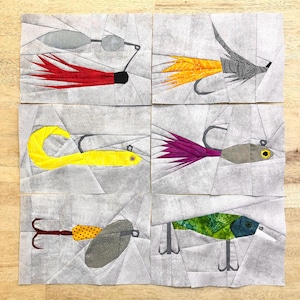 Puede incluir: Seis diseños diferentes de señuelos de pesca hechos con papel troquelado. Los señuelos están hechos de varios colores y patrones, incluyendo rojo, amarillo, verde, morado y negro. Todos los señuelos están sobre un fondo blanco.