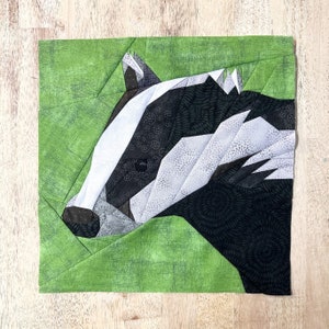 Puede incluir: Primer plano de un tejón hecho con papel y tela negra, blanca y gris. El tejón está sobre un fondo verde.