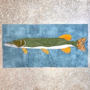 May include: A patchwork quilt depicting a green and white fish with yellow fins and a brown tail. The fish is swimming in a blue background.