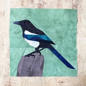 May include: A paper pieced patchwork quilt block featuring a black and white magpie perched on a brown post against a green background.