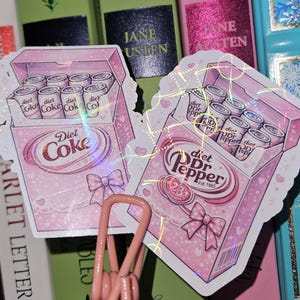 May include: Two stickers featuring pink boxes of Diet Coke and Diet Dr. Pepper cans. The Diet Coke box has a bow and the text "Diet Coke." The Diet Dr. Pepper box has the text "Diet Dr. Pepper" and "Est. 1985."