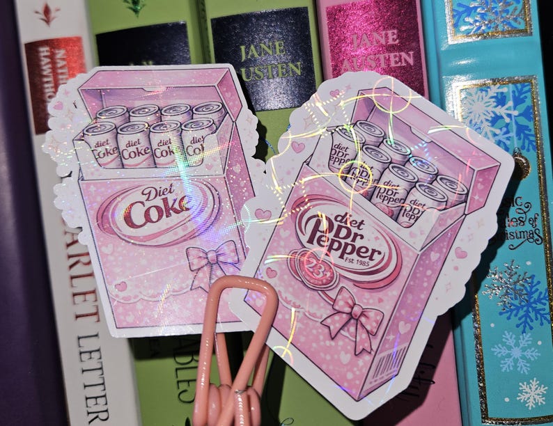 May include: Two stickers featuring pink boxes of Diet Coke and Diet Dr. Pepper cans. The Diet Coke box has a bow and the text "Diet Coke." The Diet Dr. Pepper box has the text "Diet Dr. Pepper" and "Est. 1985."