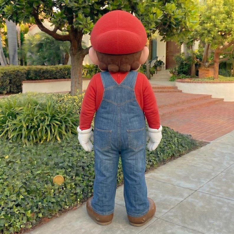 Pu&ograve; includere: Una persona con un costume di Mario, vista da dietro, &egrave; in piedi su un marciapiede. Il costume comprende un cappello rosso, una maglia rossa a maniche lunghe, una salopette di jeans blu, guanti bianchi e scarpe marroni. La persona &egrave; in un'area residenziale.