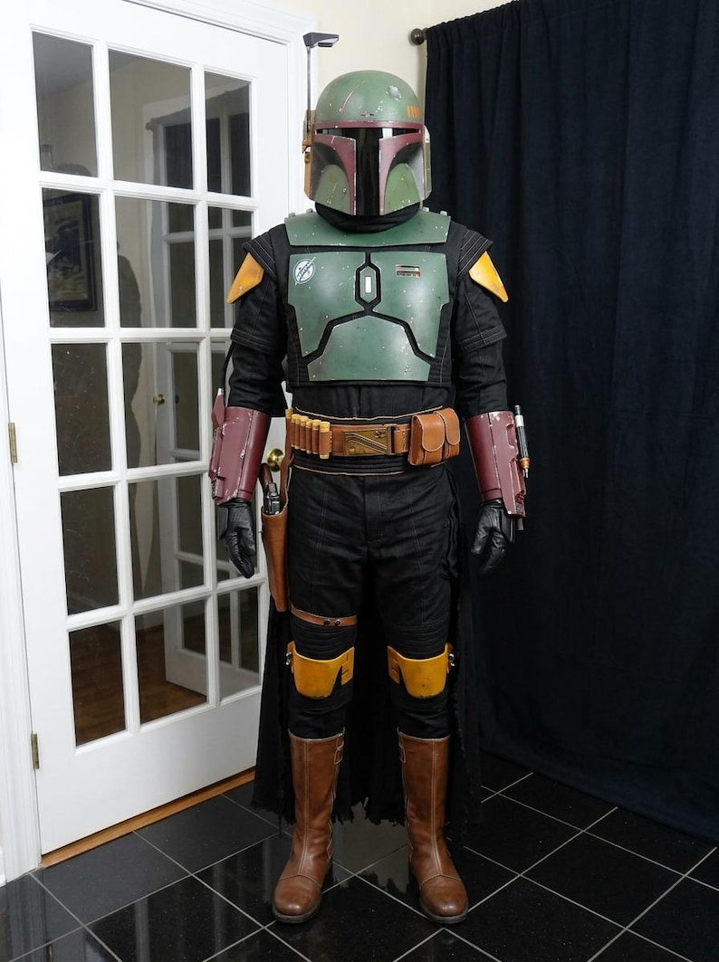 K&ouml;nnte beinhalten: Ganzk&ouml;rperkost&uuml;m, das Boba Fett aus Star Wars &auml;hnelt. Das Kost&uuml;m hat einen gr&uuml;nen Helm, eine Brustpanzerung und einen schwarzen Overall mit braunen Stiefeln. Details sind ein G&uuml;rtel mit Taschen, Panzerhandschuhe und Kniesch&uuml;tzer.