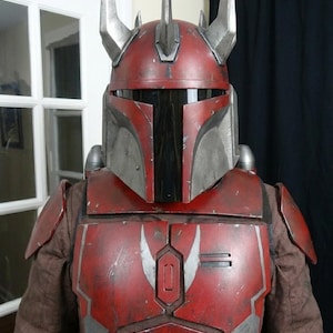 Puede incluir: Un casco y armadura Mandalorian rojos y plateados. El casco presenta una visera en forma de T y cuernos plateados. La armadura es de color rojo desgastado con detalles plateados. El disfraz est&aacute; dise&ntilde;ado para cosplay o exhibici&oacute;n.