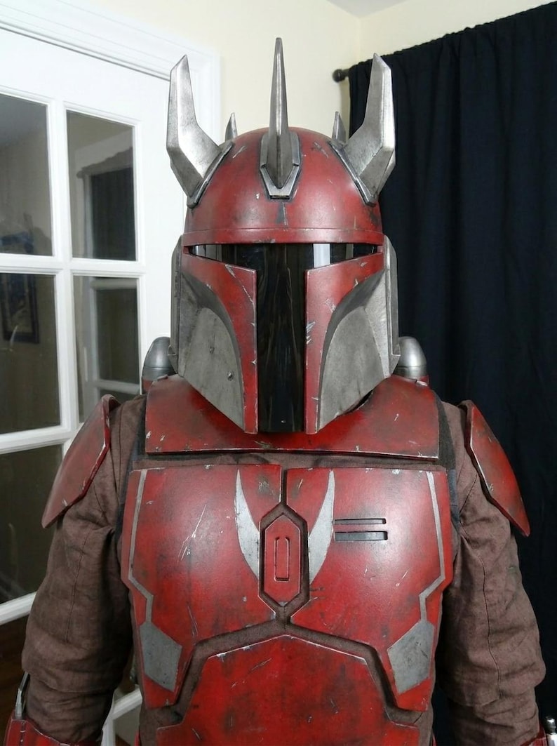 Puede incluir: Un casco y armadura Mandalorian rojos y plateados. El casco presenta una visera en forma de T y cuernos plateados. La armadura es de color rojo desgastado con detalles plateados. El disfraz est&aacute; dise&ntilde;ado para cosplay o exhibici&oacute;n.