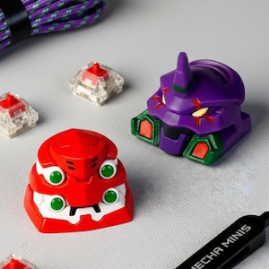 May include: A selection of colourful keycaps, including a red and white keycap with green accents, and a purple keycap with green and red accents. The keycaps have a robotic design. The text "MECHA MINIS" is visible on a black object.