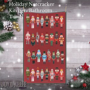 May include: A red kitchen or bathroom towel with a pattern of colorful nutcracker figurines. The towel has the text "Holiday Nutcracker Kitchen/Bathroom Towel" at the top and "Joy McKee Prints" at the bottom.
