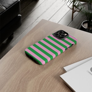 Puede incluir: Una funda para teléfono de rayas rosas y verdes con un recorte para el objetivo de la cámara negro.