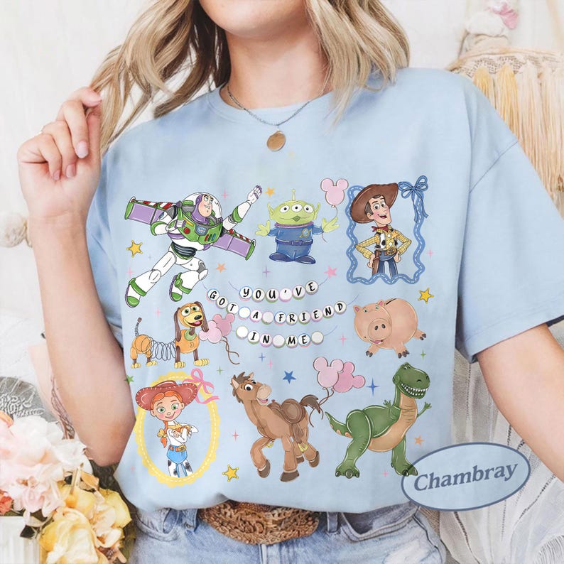Pu&ograve; includere: T-shirt azzurra con illustrazioni colorate dei personaggi del film "Toy Story". Il design include Buzz Lightyear, Woody e altri personaggi, con la scritta "YOU'VE GOT A FRIEND IN ME."