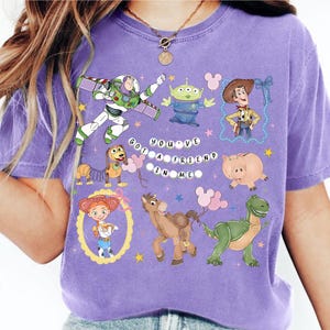 Pu&ograve; includere: Una maglietta viola con vari personaggi dei cartoni animati, tra cui Buzz Lightyear, Woody e un alieno verde. La frase "YOU'VE GOT A FRIEND IN ME" &egrave; stampata in bianco. La maglietta ha un girocollo e maniche corte.