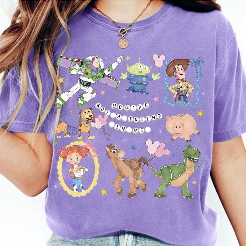 Pu&ograve; includere: Una maglietta viola con vari personaggi dei cartoni animati, tra cui Buzz Lightyear, Woody e un alieno verde. La frase "YOU'VE GOT A FRIEND IN ME" &egrave; stampata in bianco. La maglietta ha un girocollo e maniche corte.