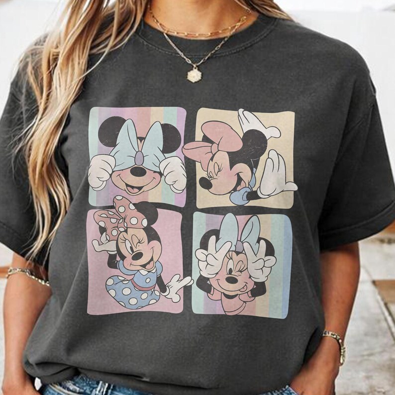 May include: Dark gray t-shirt featuring four squares with different Minnie Mouse poses. Each square has a pastel striped background. Minnie is wearing different colored bows and outfits in each square.