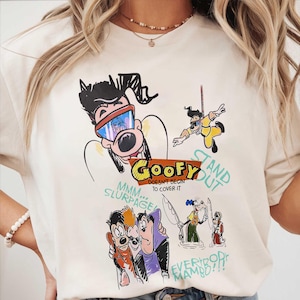 May include: Cream-colored t-shirt featuring a cartoon graphic of Goofy and other characters. The graphic includes the word "Goofy" in yellow and red, along with the phrases "Stand Out" and "Everybody Mambo!!!".