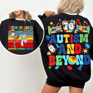May include: Black sweatshirt with a colorful graphic promoting autism awareness. The design includes the text "Autism Awareness And Beyond", puzzle pieces, a rocket, and the characters Woody and Buzz Lightyear.