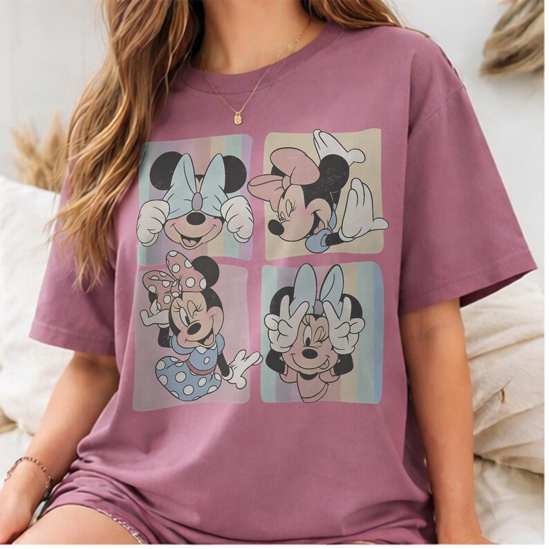 May include: Mauve-colored t-shirt featuring a four-panel graphic of Minnie Mouse in various poses. Each panel has a pastel rainbow background. Minnie is depicted with her hands covering her eyes, holding her face, and making a peace sign.