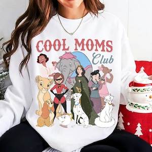 May include: White sweatshirt with the text "COOL MOMS CLUB" in red and blue. The graphic features cartoon characters including a lion cub, a dalmatian, and a cat. The sweatshirt is a crew neck style.