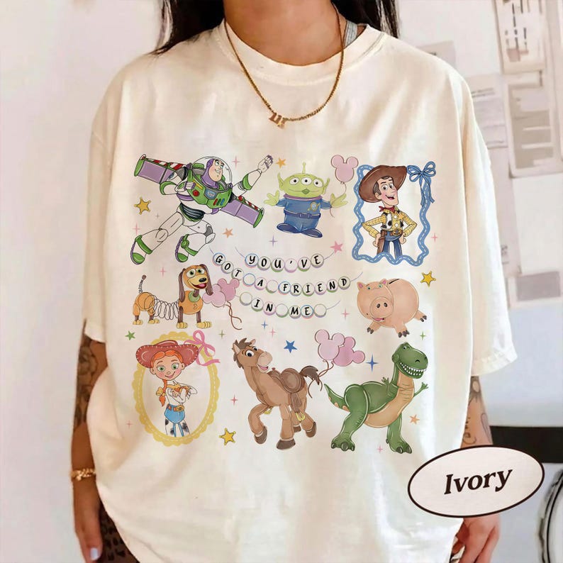 Pu&ograve; includere: T-shirt color avorio con personaggi di cartoni animati di un popolare film. Il design include Buzz Lightyear, un alieno, Woody, Jessie, Slinky Dog, Hamm, Bullseye e Rex, con la scritta "You've Got a Friend in Me."