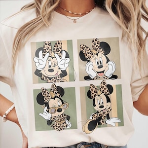 Könnte beinhalten: Cremefarbenes T-Shirt mit einem vierteiligen Design von Minnie Mouse in verschiedenen Posen. Jede Minnie Mouse-Illustration hat eine Schleife und ein Outfit mit Leopardenmuster. Der Hintergrund hat vertikale Streifen in Beige und Grün.