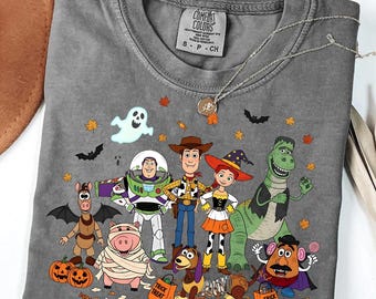 Può includere: Una t-shirt girocollo grigio antracite con una stampa grafica di vari personaggi dei cartoni animati vestiti con costumi di Halloween, tra cui un fantasma, pipistrelli e zucche, con l'etichetta Comfort Colors visibile sul collo.
