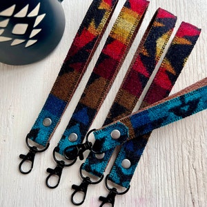 May include: Five colorful keychains with a southwestern pattern and black metal key rings. The keychains are made of fabric and have a leather backing.