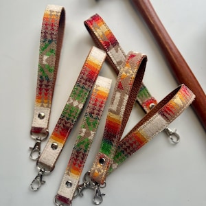 May include: Five colorful keychains with a southwestern pattern and silver key rings. The keychains are made of fabric and have a leather backing.