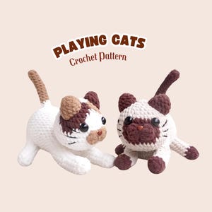 May include: Two crocheted cat figures in white, brown, and tan. One cat is in a playful pose, the other is sitting. The text "PLAYING CATS Crochet Pattern" is displayed above the cats.