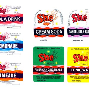 May include: Six different vintage soda labels featuring a fairy and the brand name "She" in red. The labels are for Cola Drink, Cream Soda, Dandelion & Burdock, Lemonade, Limeade, and American Ginger Ale.