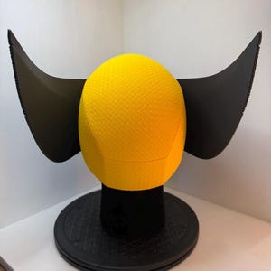 Peut inclure: Une sph&egrave;re jaune textur&eacute;e avec des extensions noires en forme d'ailes, mont&eacute;e sur une base circulaire noire. La sph&egrave;re pr&eacute;sente un motif en losange. L'objet est une pi&egrave;ce d&eacute;corative, peut-&ecirc;tre une sculpture ou un objet d'exposition unique.